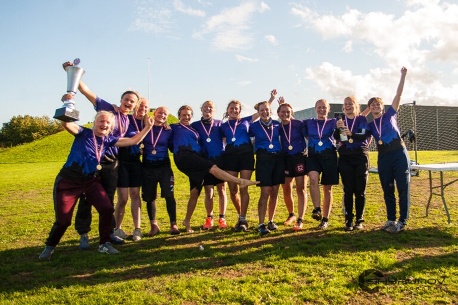 Aarhus Ultimate team celebrates victory outdoors holding trophy and medals on sunlit grass.