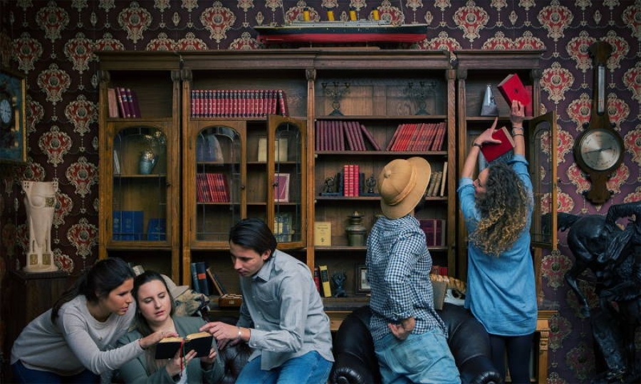 TeamEscape SPACE ESCAPE in Ulm features a group of individuals seated around a bookcase, sharing ideas.