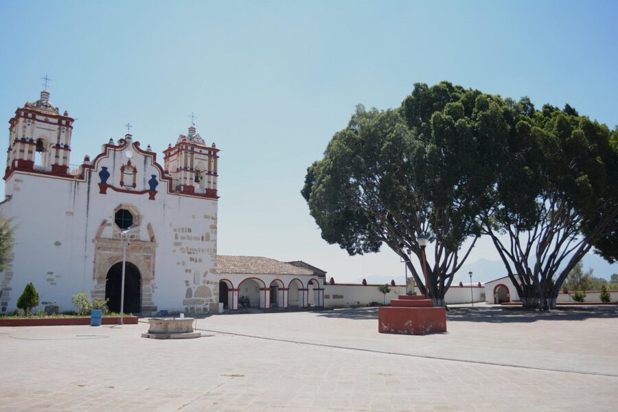 Preciosa Sangre de Cristo Church, a large white building in Teotitlán del Valle, Mexico, framed by a large tree.

