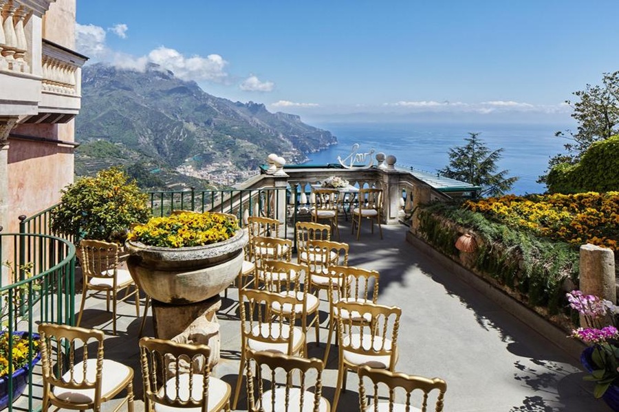 Palazzo Avino terrace with golden chairs overlooking Amalfi Coast, surrounded by gardens and mountains.