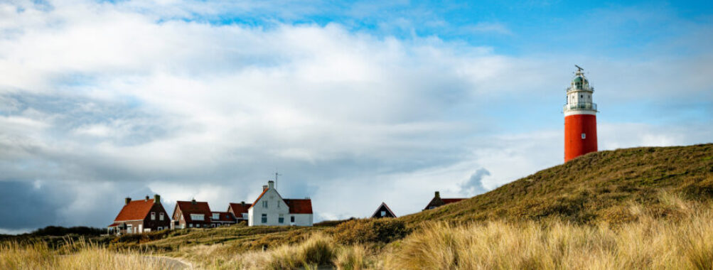 Lighthouse on Texel Island in Holland, standing tall against a clear blue sky, surrounded by sandy dunes and grass.