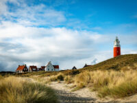Lighthouse on Texel Island in Holland, standing tall against a clear blue sky, surrounded by sandy dunes and grass.