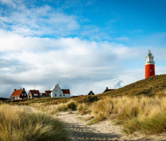 Lighthouse on Texel Island in Holland, standing tall against a clear blue sky, surrounded by sandy dunes and grass.