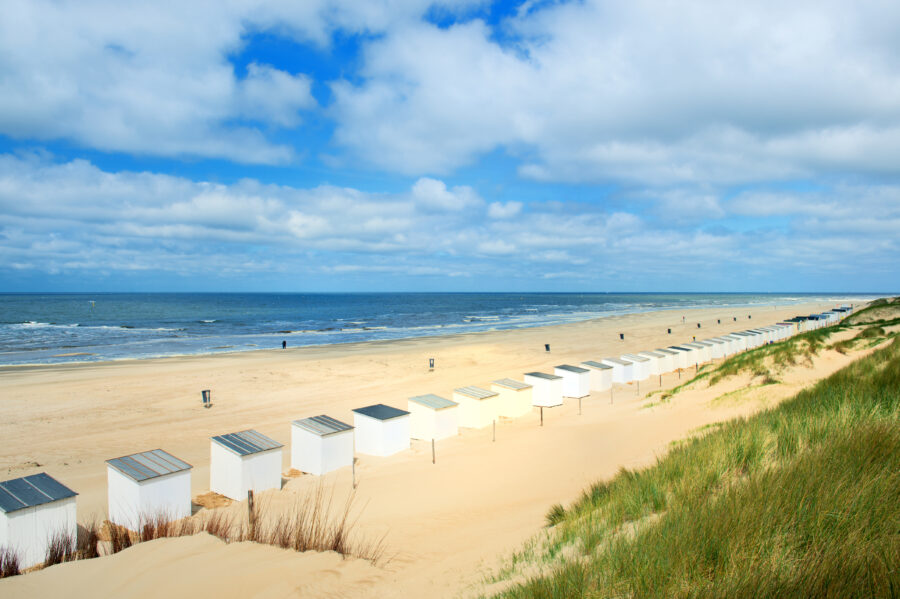 Blue beach huts lined along the sandy shore of Texel Island, Netherlands, with a clear blue sky in the background.