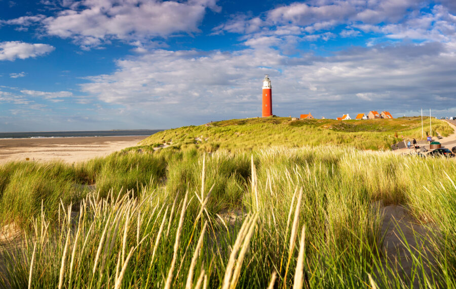 Bright sunlight during sunset highlights the iconic red lighthouse on Texel Island, The Netherlands, against a colorful sky