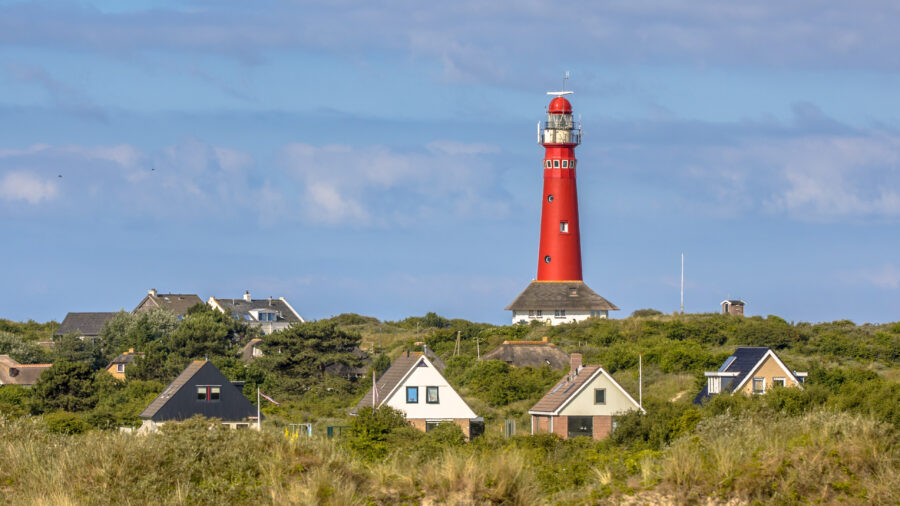 Scenic view of Texel Island village with a prominent lighthouse against a clear blue sky.