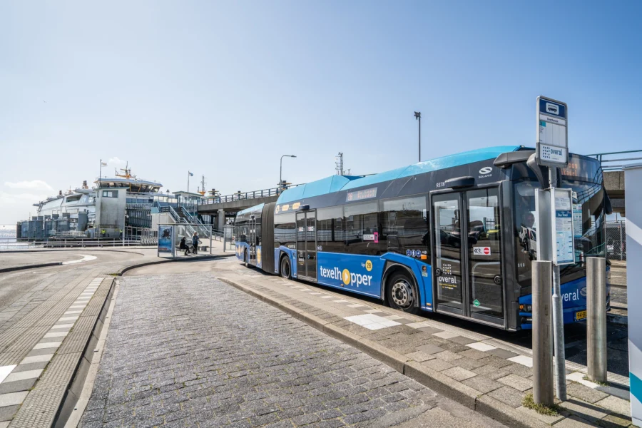 Texelhopper bus at Dutch ferry terminal, coastal public transportation hub on sunny day.
