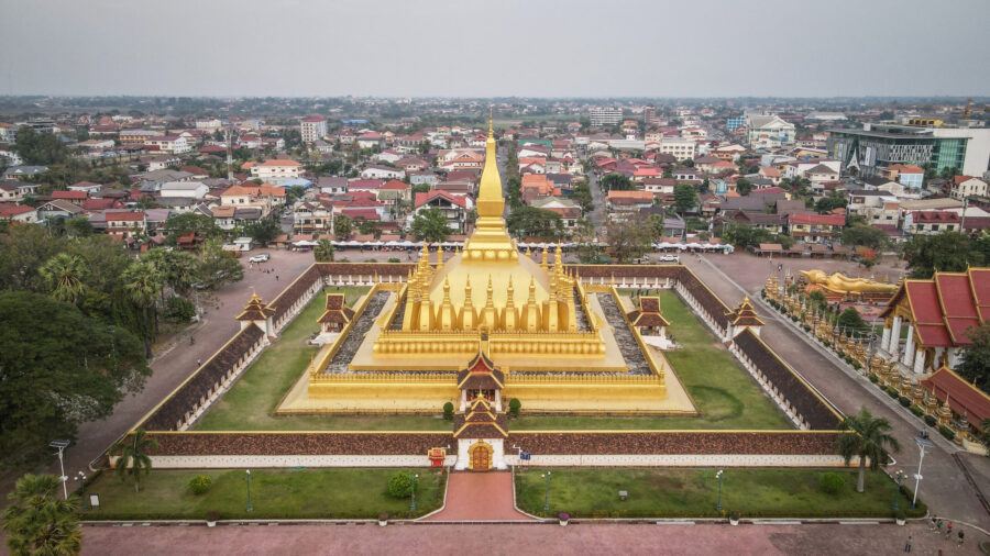 Aerial view of Pha That Luang Stupa, Vientianes golden landmark amidst urban landscape.