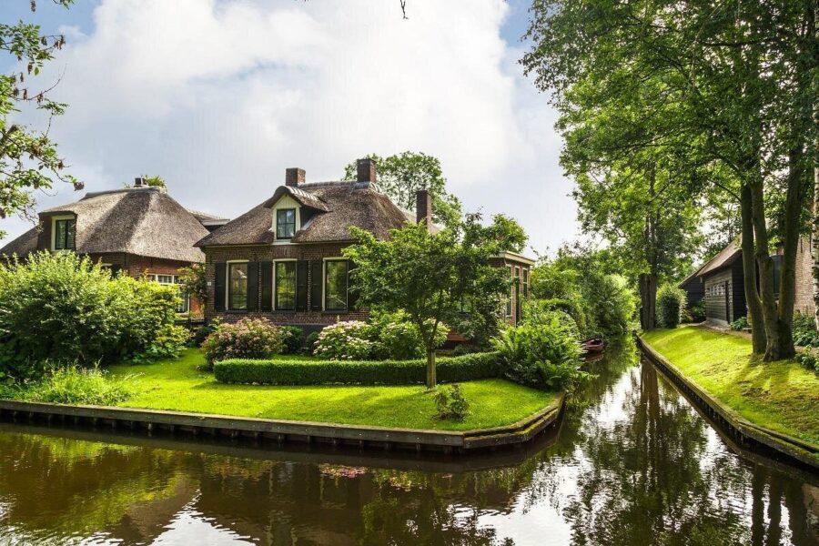 Thatched cottage beside tranquil canal with boat, garden, and reflective water.