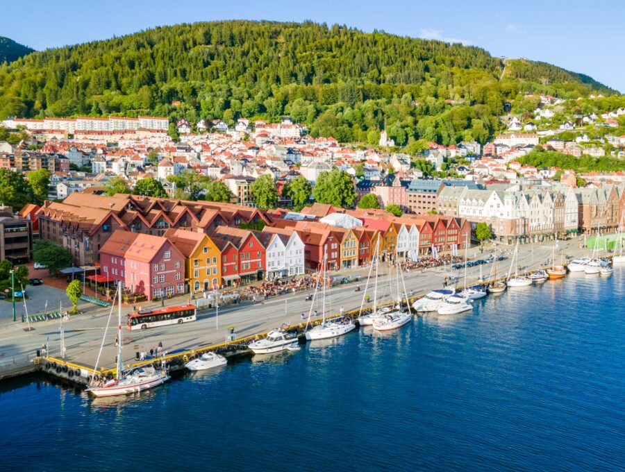 Charming coastal town in Norway with colorful buildings, sailboats, and lush green hills.