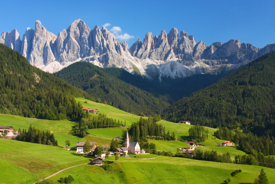 Scenic view of the Dolomites in the European Alps, characterized by towering peaks and vibrant green valleys beneath a bright sky