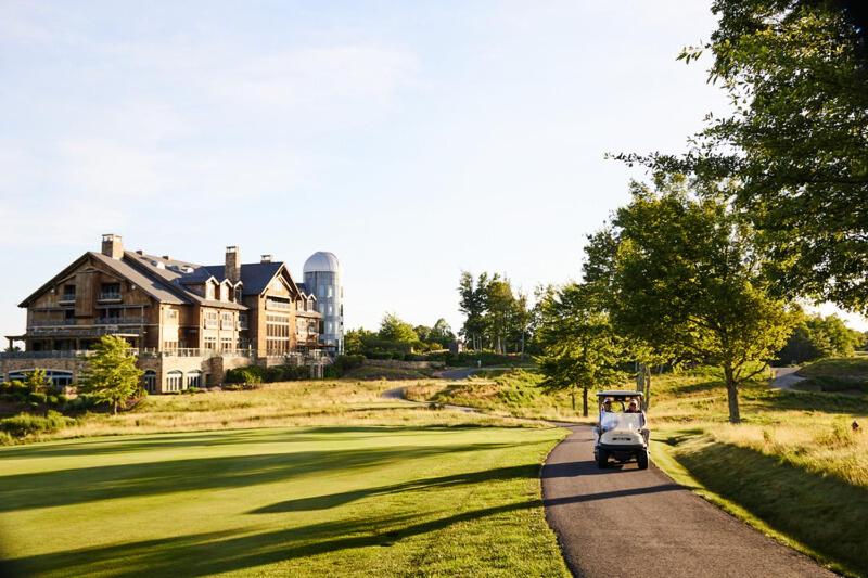 Golf cart drives down a scenic path near a large house at The Lodge at Primland, part of the Auberge Collection.