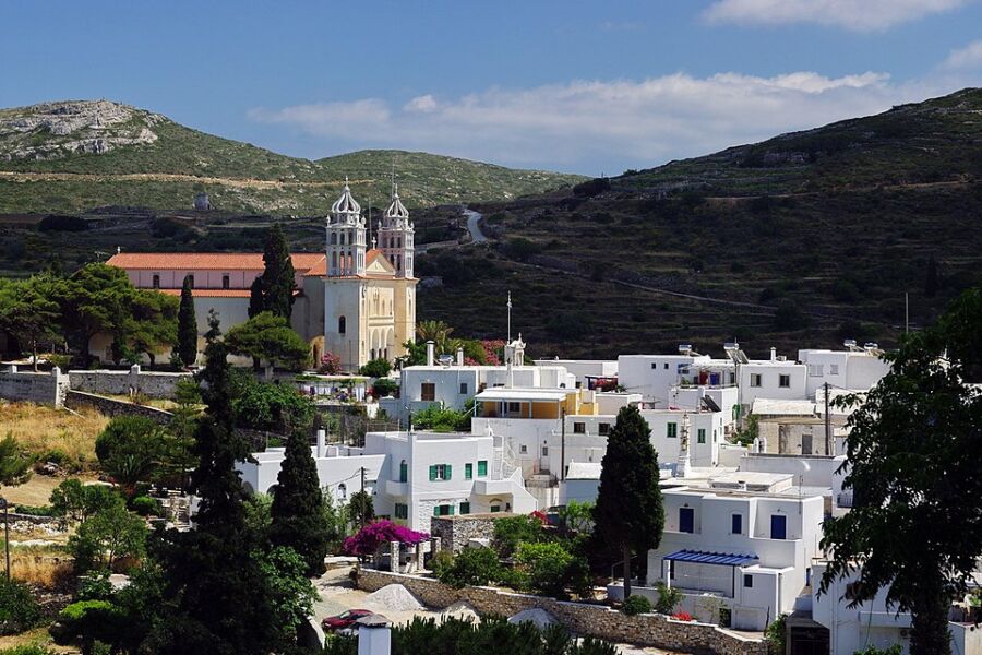 Ppicturesque church with a tower overlooks Piso Livadi, Greece, perched on a hill with scenic views of the landscape.