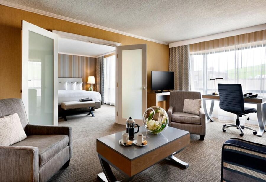 Interior of a hotel room at The Prince George Hotel, showcasing a couch, chair, and a television for relaxation.