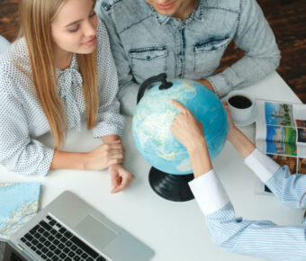 Travel agent discussing vacation plans with a young couple in a tour agency, showcasing travel destination options.