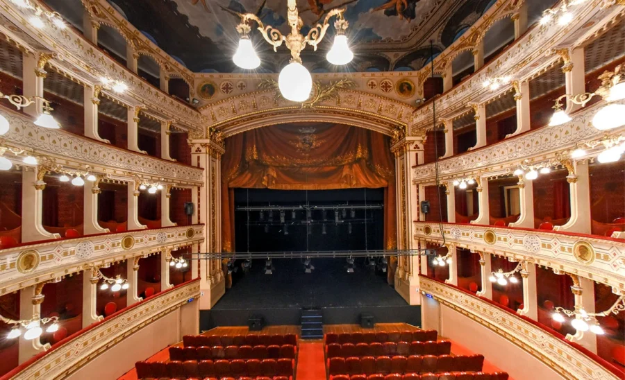 Ornate classical theater interior with gilded decorations and plush red seating.