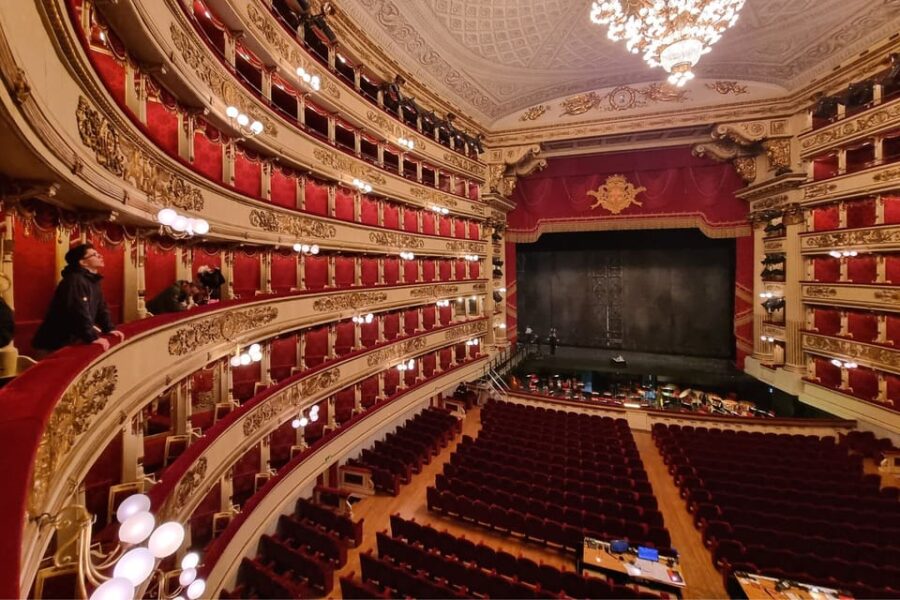 Luxurious opera house interior with grand chandelier, rich reds, gold accents, and plush seating.