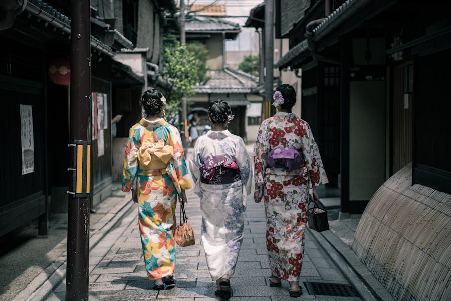 Three women in colorful kimonos walking down a traditional Japanese stone lane.