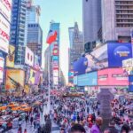 Times Square NYC bustling with vibrant crowds, colorful billboards, yellow taxis, and diverse architecture.