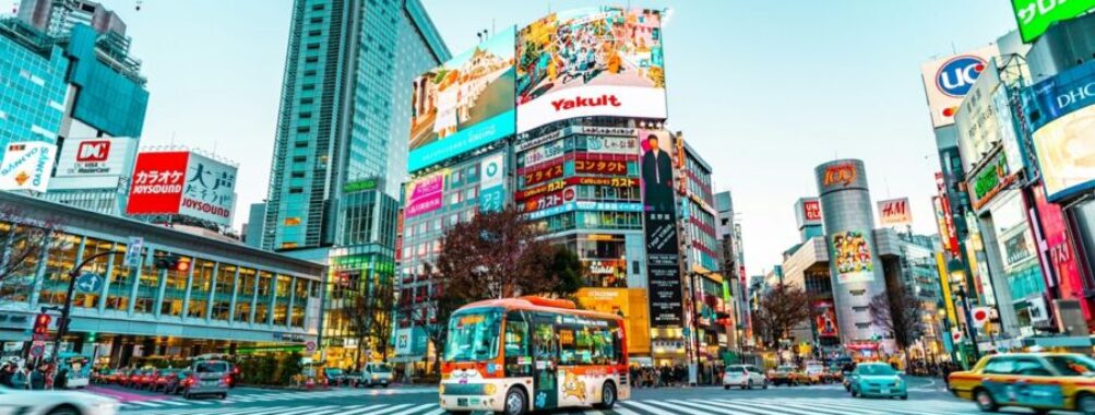 Bustling Tokyo intersection with skyscrapers, vibrant ads, and colorful bus at twilight.