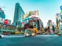 Bustling Tokyo intersection with skyscrapers, vibrant ads, and colorful bus at twilight.