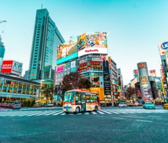Bustling Tokyo intersection with skyscrapers, vibrant ads, and colorful bus at twilight.