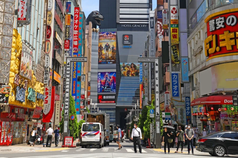 Tokyo Kabukicho entertainment street with Godzilla head, neon signs, Hotel Gracery in daylight.