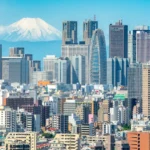 Cityscape of Shinjuku, Tokyo, with modern buildings in the foreground and Mt. Fuji rising majestically in the background.