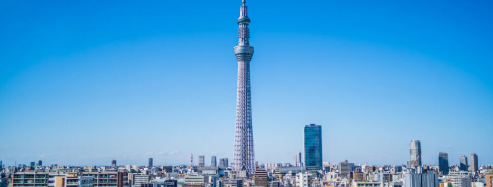 Tokyo skyline with the iconic Skytree tower centered, surrounded by modern buildings under a clear blue sky, conveying a sense of urban vibrancy.