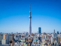 Tokyo skyline with the iconic Skytree tower centered, surrounded by modern buildings under a clear blue sky, conveying a sense of urban vibrancy.