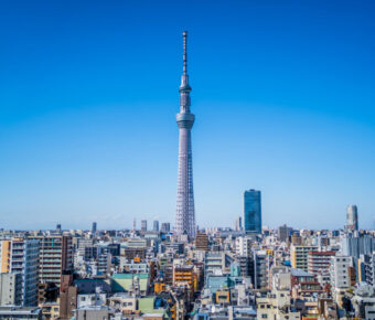 Tokyo skyline with the iconic Skytree tower centered, surrounded by modern buildings under a clear blue sky, conveying a sense of urban vibrancy.