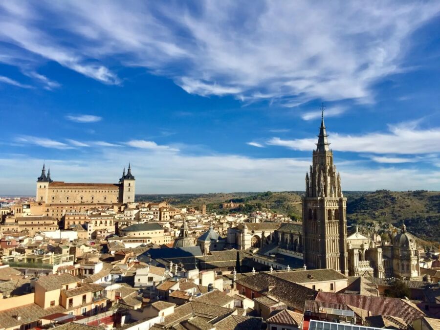 Scenic view of Toledo, Spain, featuring the Alcázar and Toledo Cathedral with a vivid blue sky and wispy clouds, creating a serene atmosphere.