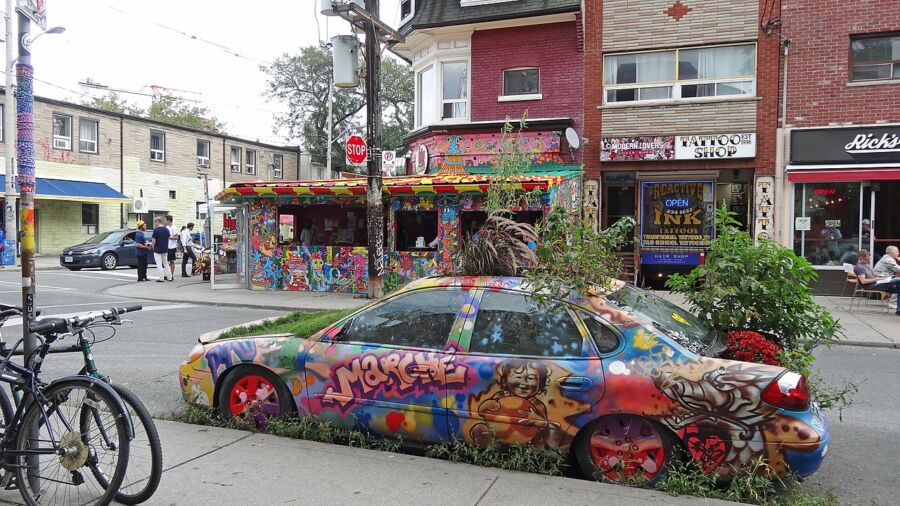 Colorful, graffiti-decorated car is parked along the road in Kensington Market, Toronto, highlighting urban art culture.