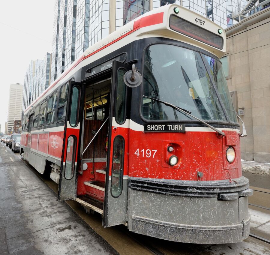 Toronto streetcar stops at a station, with passengers boarding and disembarking on a busy city street.
