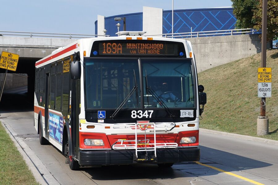 Toronto Transit Commission bus drives down a street with a tunnel visible in the background.
