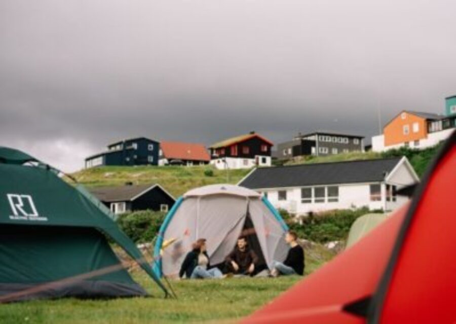 People sitting around a tent on grass at Tórshavn Camping, showcasing a social gathering in the Faroe Islands.