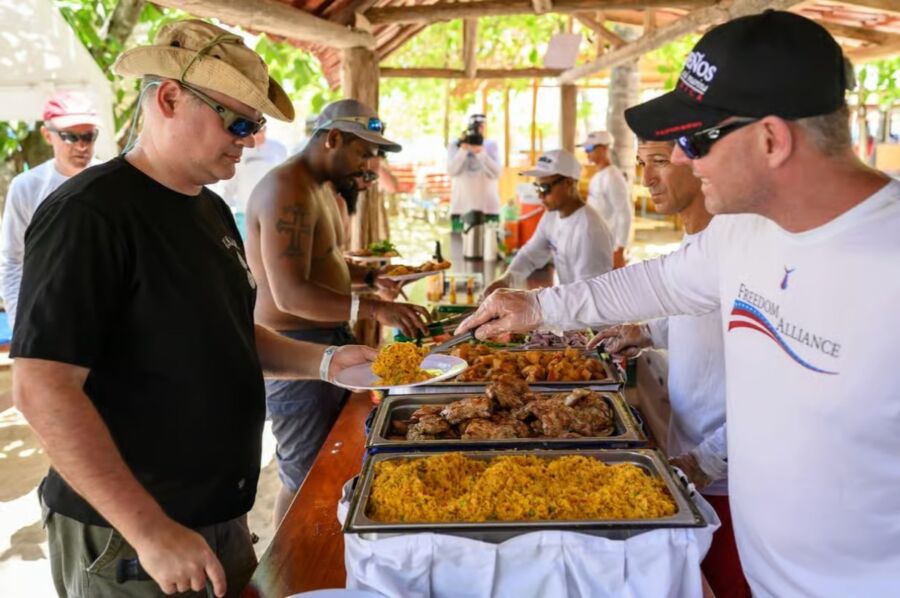 Two men serving food at a buffet during the Tortuga Beach Day Trip, with guests eagerly waiting to be served.