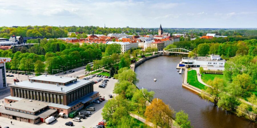 Aerial view of Tartu riverfront with arched bridge, red-roofed buildings, and riverside park.