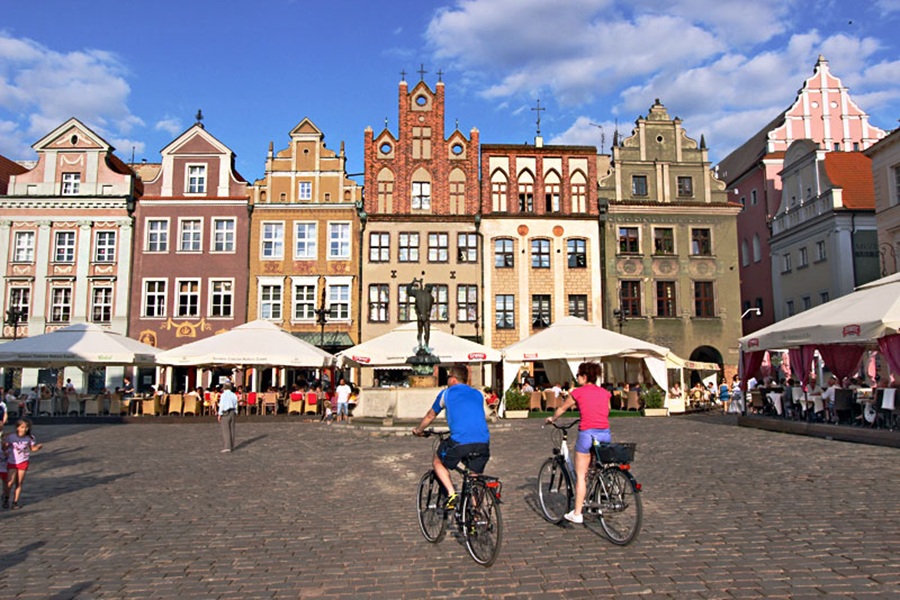 Poznań Old Market Square, Poland, cyclists, cafes, fountain, cobblestone historic townhouses.
