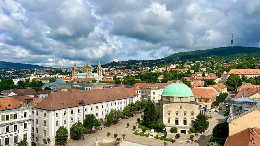 Pécs historic town square with green domed building, red tile roofs and twin church towers.