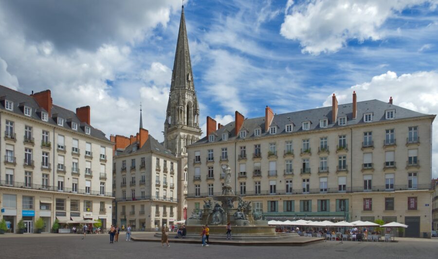 Nantes historic square with ornate fountain, church spire, and outdoor cafes.