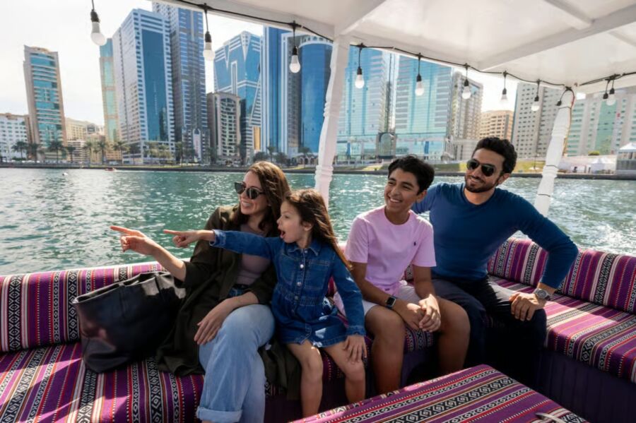 Family enjoys a traditional Abra boat tour in Sharjah’s Khalid Lagoon, with a city skyline in the background.