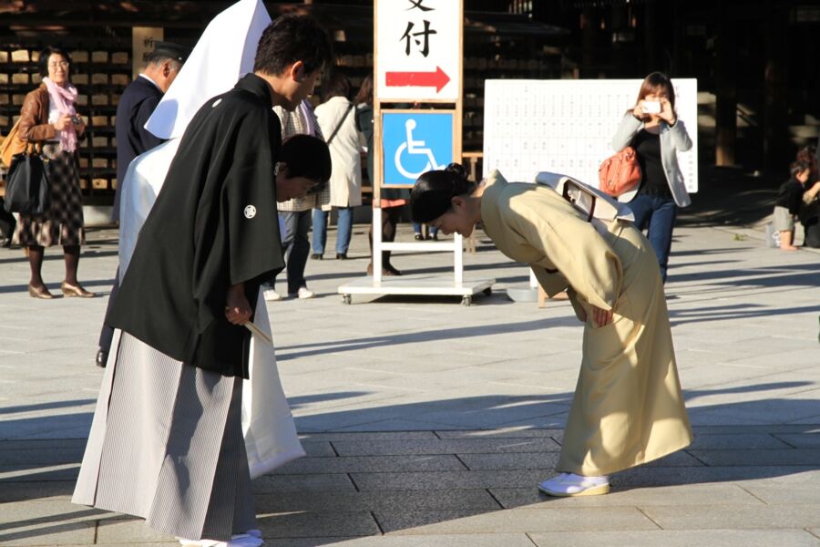 Japanese ceremony at shrine with people in kimonos bowing, blending tradition and modernity.