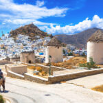 Scenic view of Ios island featuring traditional houses, windmills, churches, and a donkey in the Cyclades, Greece