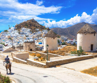 Scenic view of Ios island featuring traditional houses, windmills, churches, and a donkey in the Cyclades, Greece