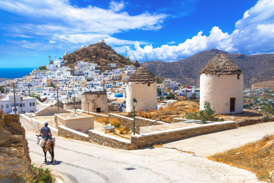 Scenic view of Ios island featuring traditional houses, windmills, churches, and a donkey in the Cyclades, Greece
