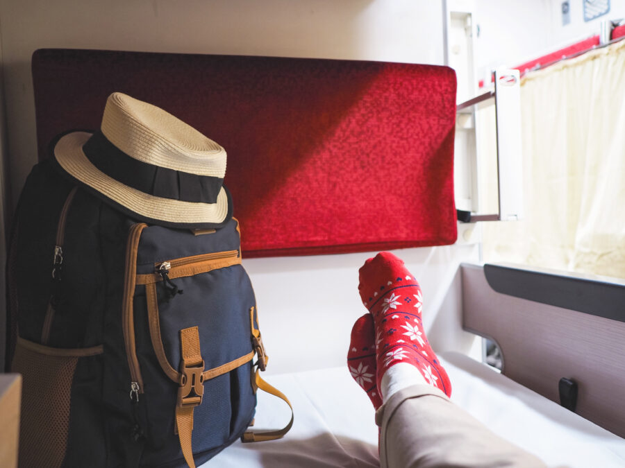 Tourist in red Christmas-patterned socks takes a selfie with a backpack and hat on a train bed.