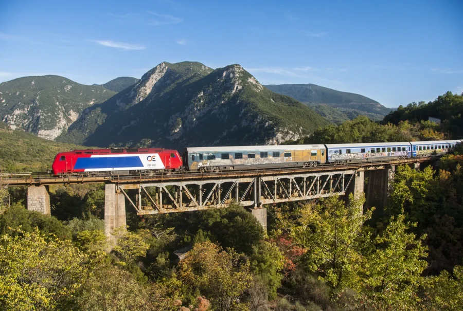 Athens to Meteora red train crossing high viaduct in Greek mountains.
