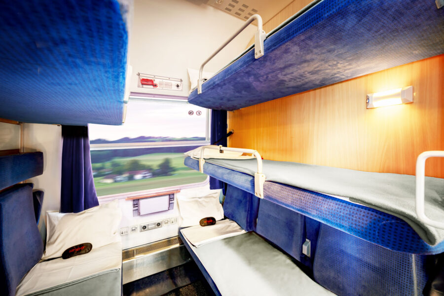 Cozy train sleeping compartment with bunk beds, wood finish, natural light, and scenic view.