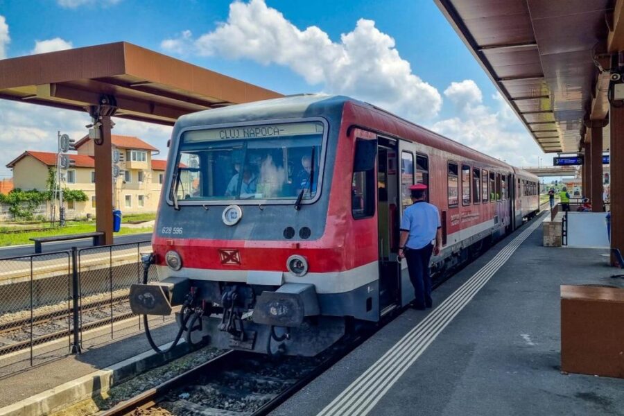 Modern red and gray passenger train at Cluj Napoca station with conductor and clear blue sky.